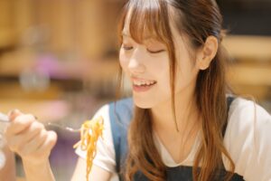 色の濃い食べ物、パスタを食べる女性